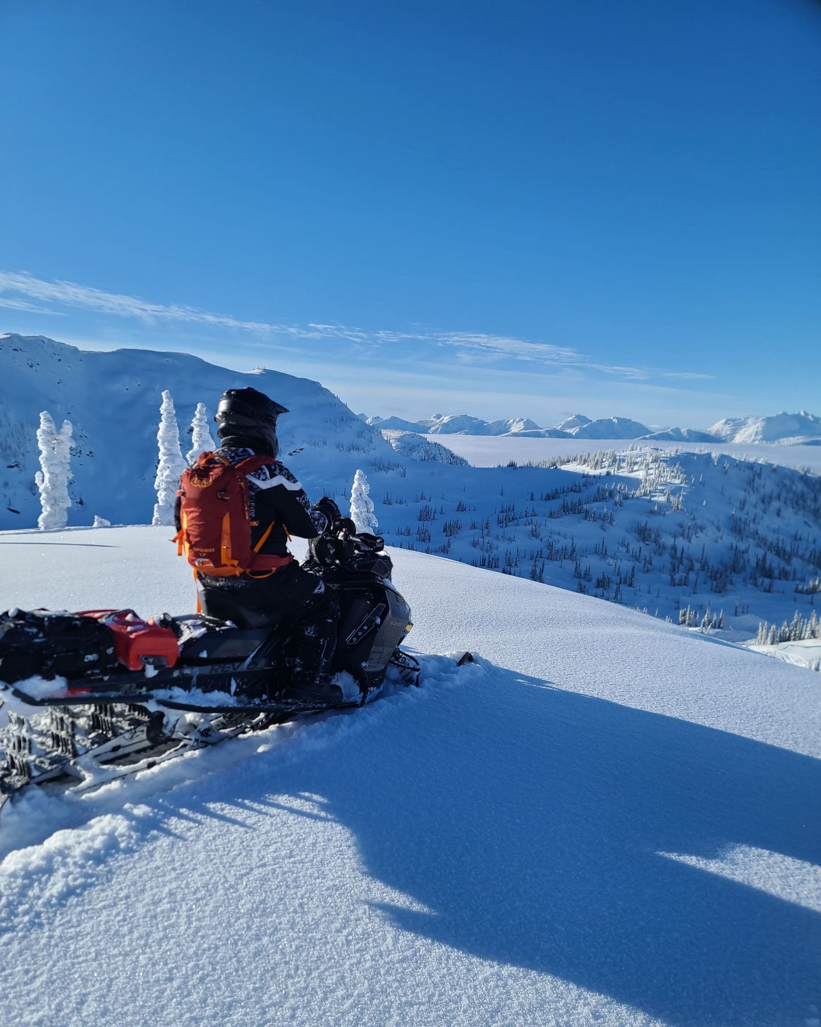 Snøscooterkjører på fjelltopp med utsikt over vinterlandskap